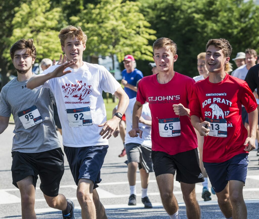 Four runners wave to camera while racing for a fundraiser