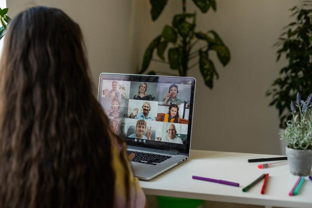 A girl is sitting at a table with a laptop during an online video chat of a school lesson with a teacher and class.