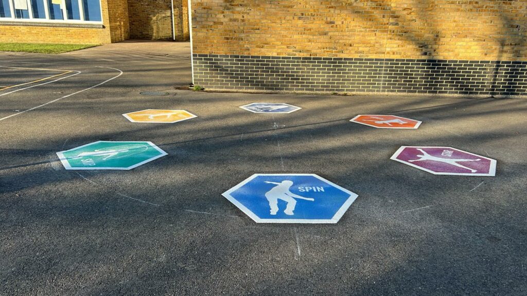 Fitness circle 1 playground markings, featuring spin hexagon. Multi-coloured hexagons in background, building behind.