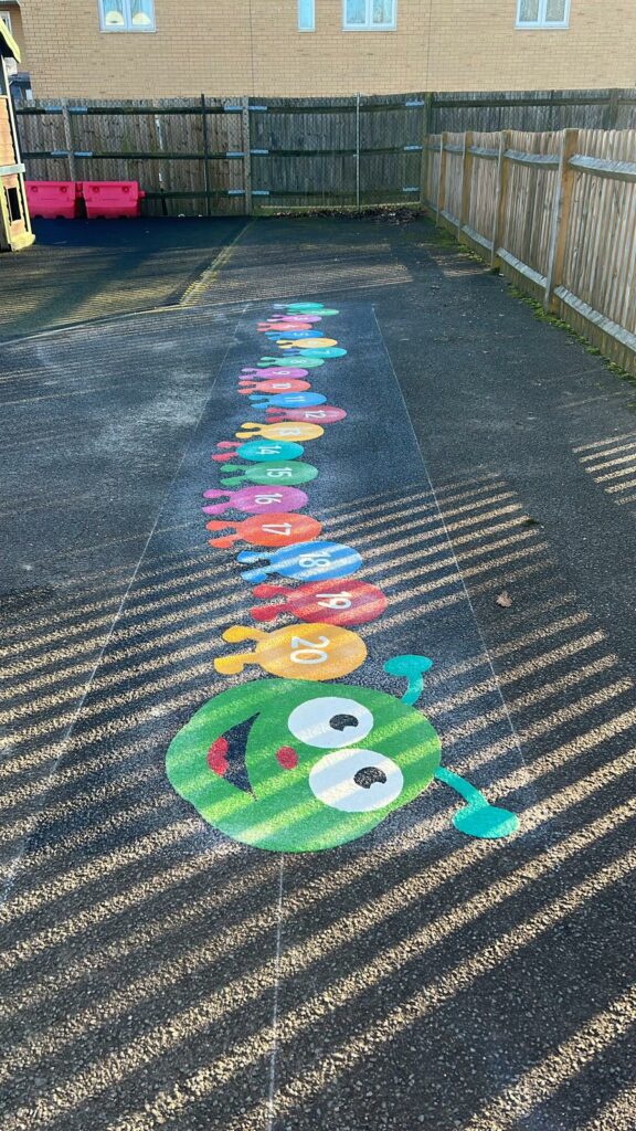 1-20 caterpillar playground markings, bins, buildings, and fences behind.