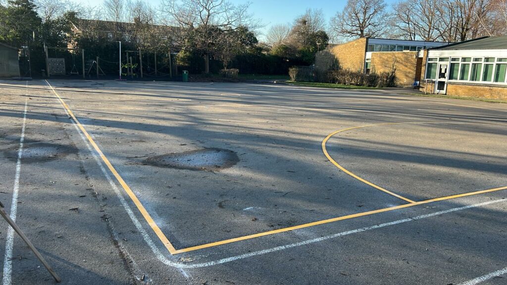 netball court playground markings, trees and green space behind.